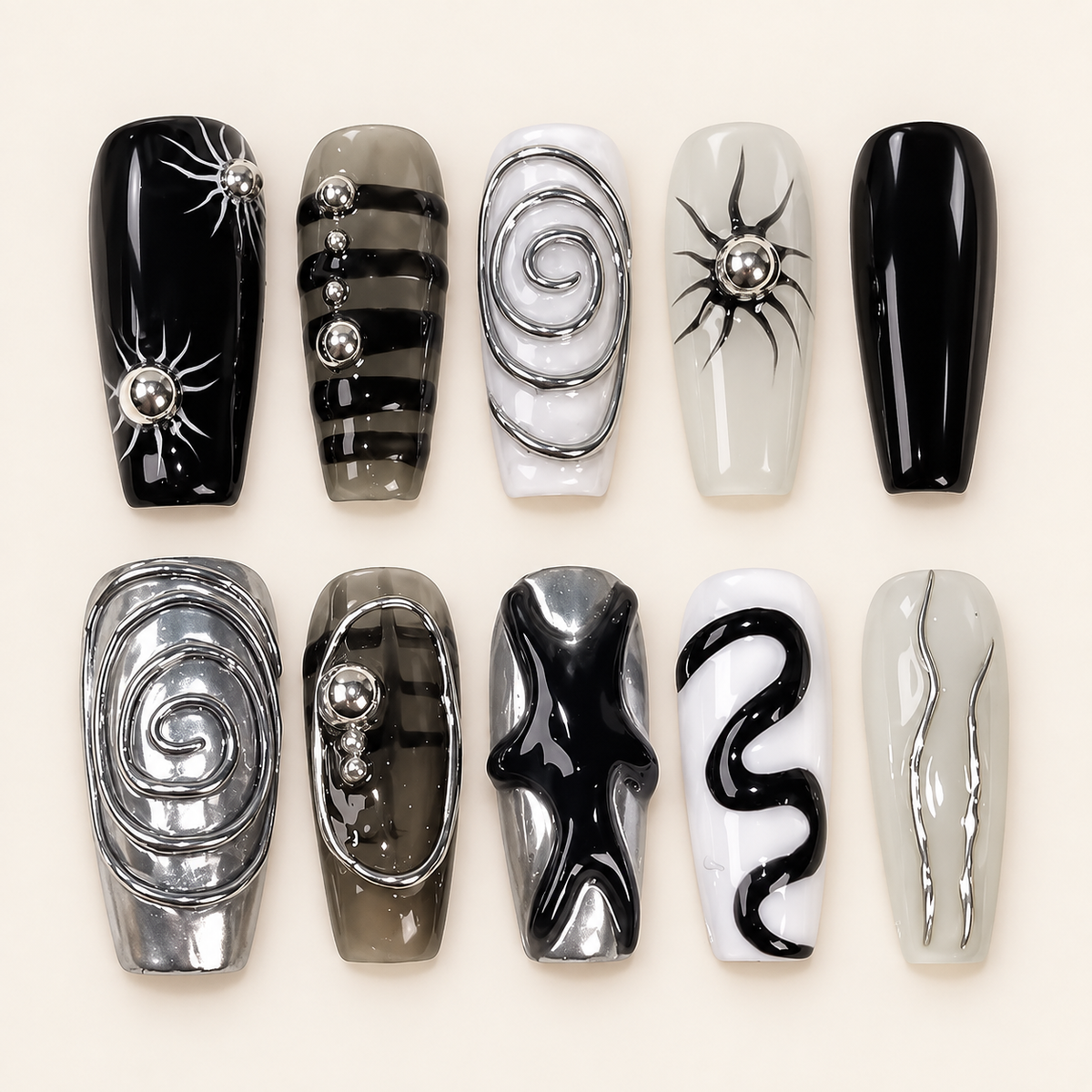 Dix press on nails coffin noirs, blancs et gris, décorés de spirales chromées, d’étoiles et de perles argentées, sur fond ivoire.