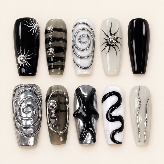 Dix press on nails coffin noirs, blancs et gris, décorés de spirales chromées, d’étoiles et de perles argentées, sur fond ivoire.
