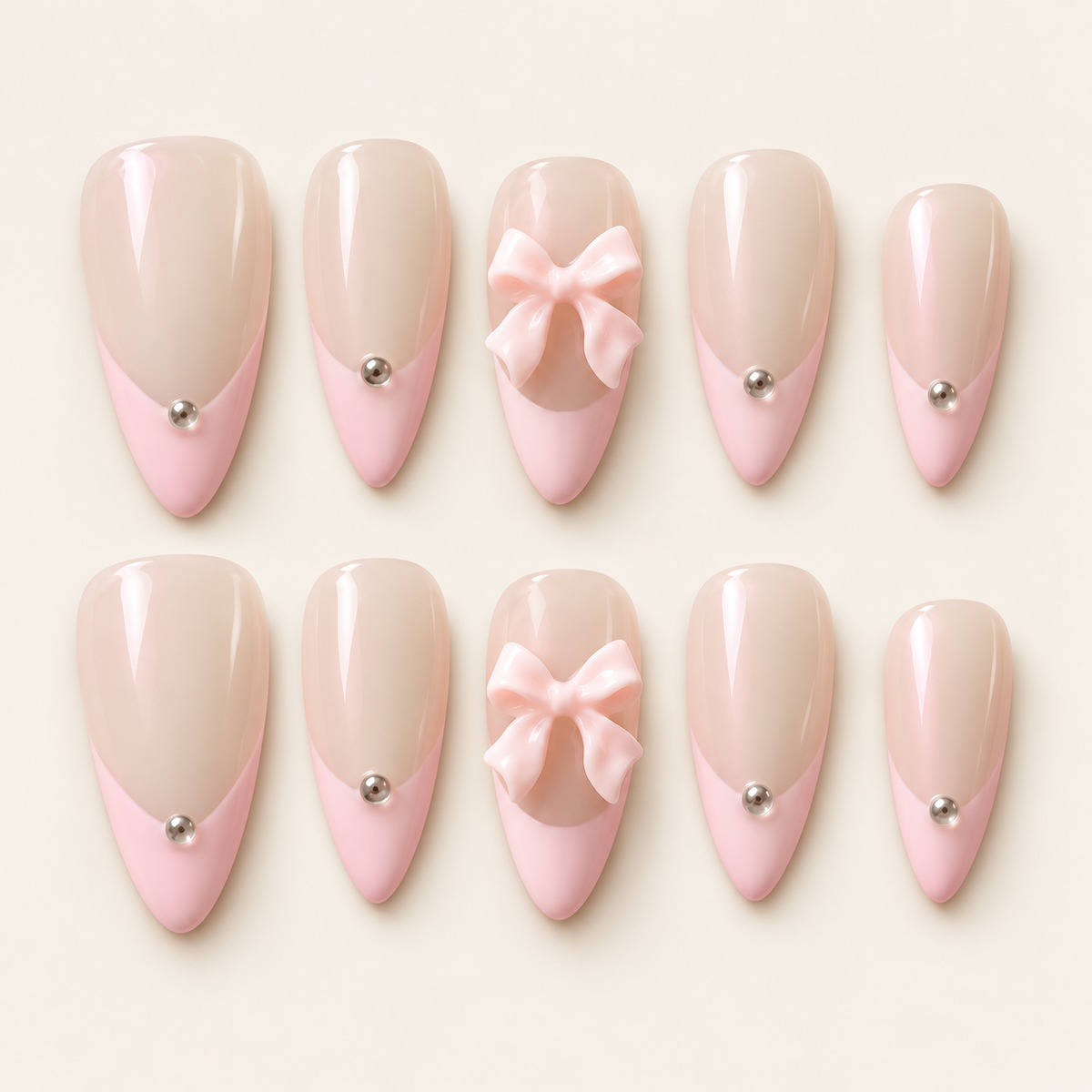 Ensemble de 10 faux ongles amande nude nacré et French rose pastel, décorés de nœuds roses 3D et de détails argentés, sur fond ivoire.