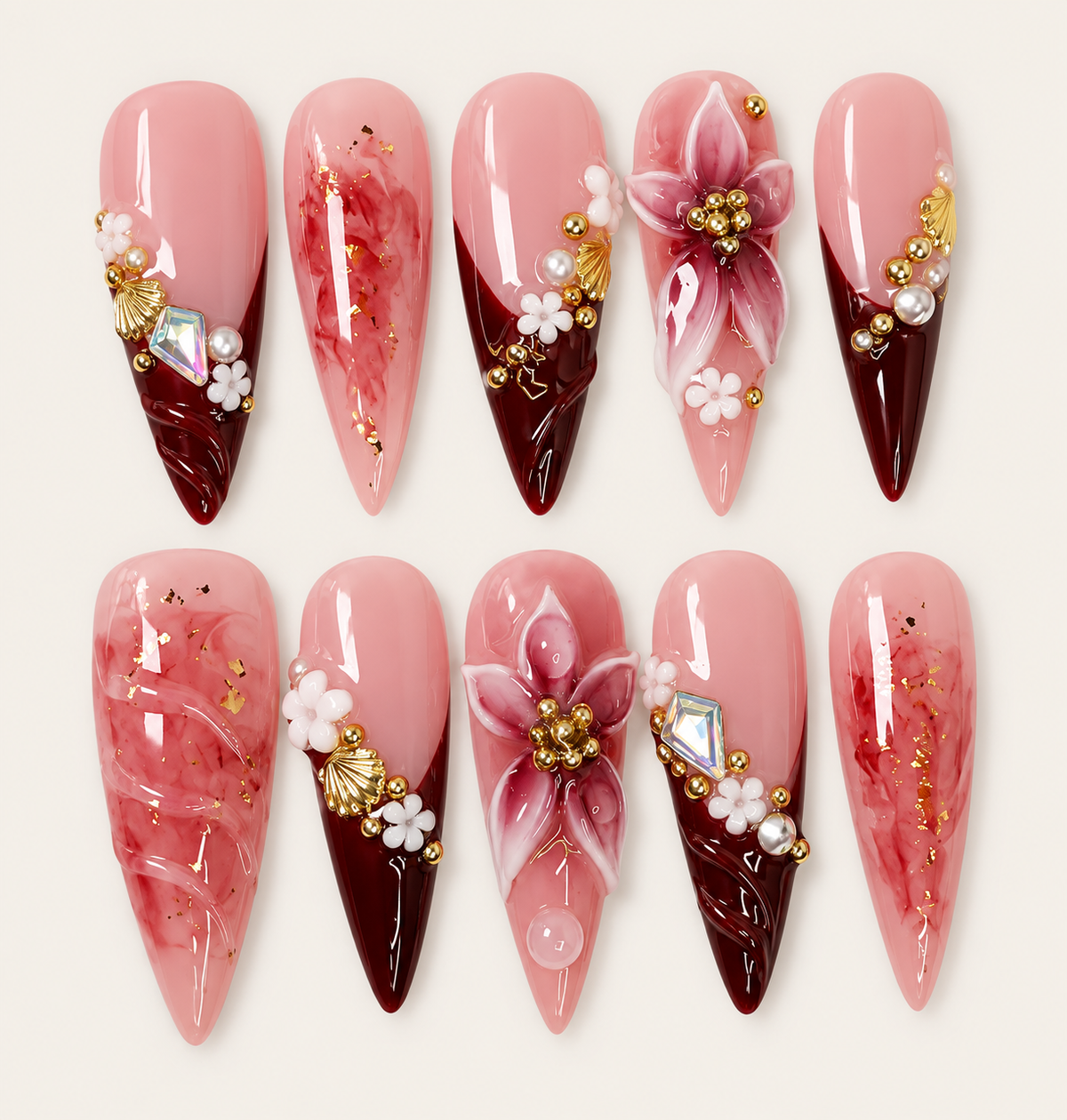 10 press-on nails Velorys longs et pointus, roses et bordeaux, avec fleurs 3D, motifs marbrés, perles et ornements dorés sur fond ivoire.