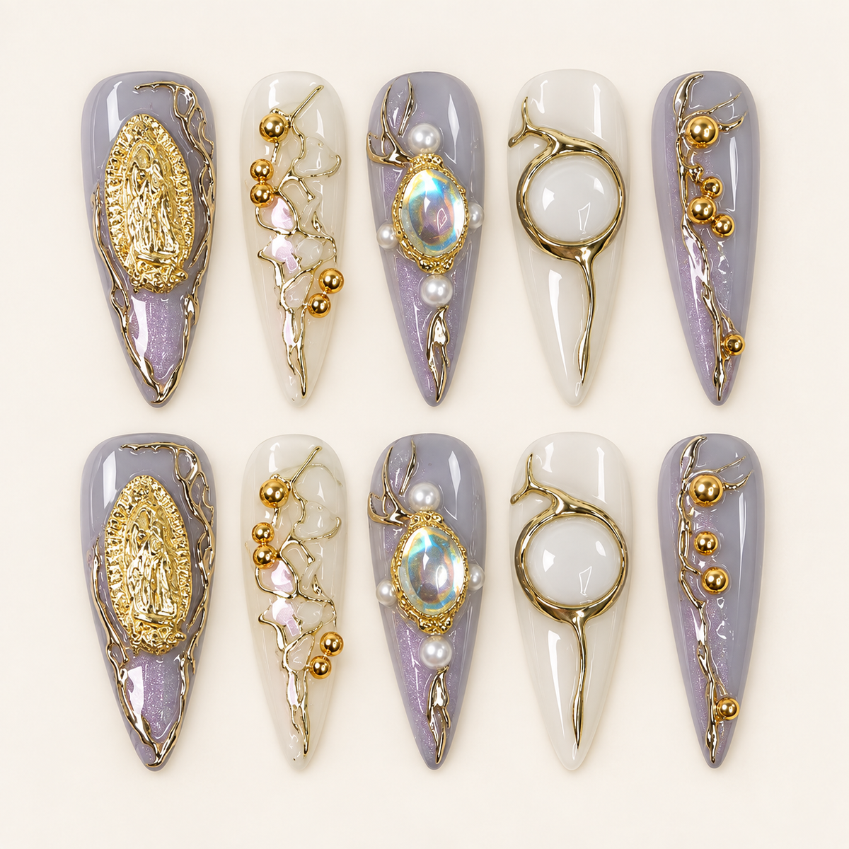 Dix press on nails longs et pointus lilas et blanc laiteux, décorés de médaillons dorés, de cabochons irisés et de perles, sur fond ivoire.